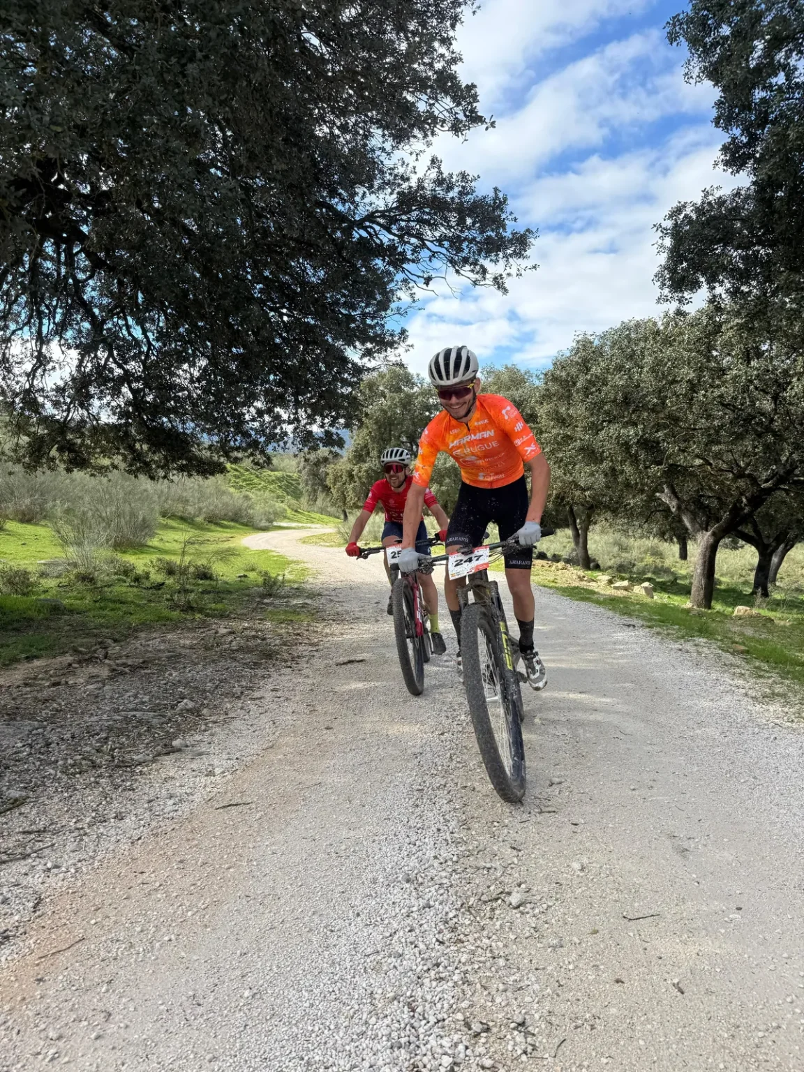 Dos ciclistas entrenando por una pista de tierra entre olivos